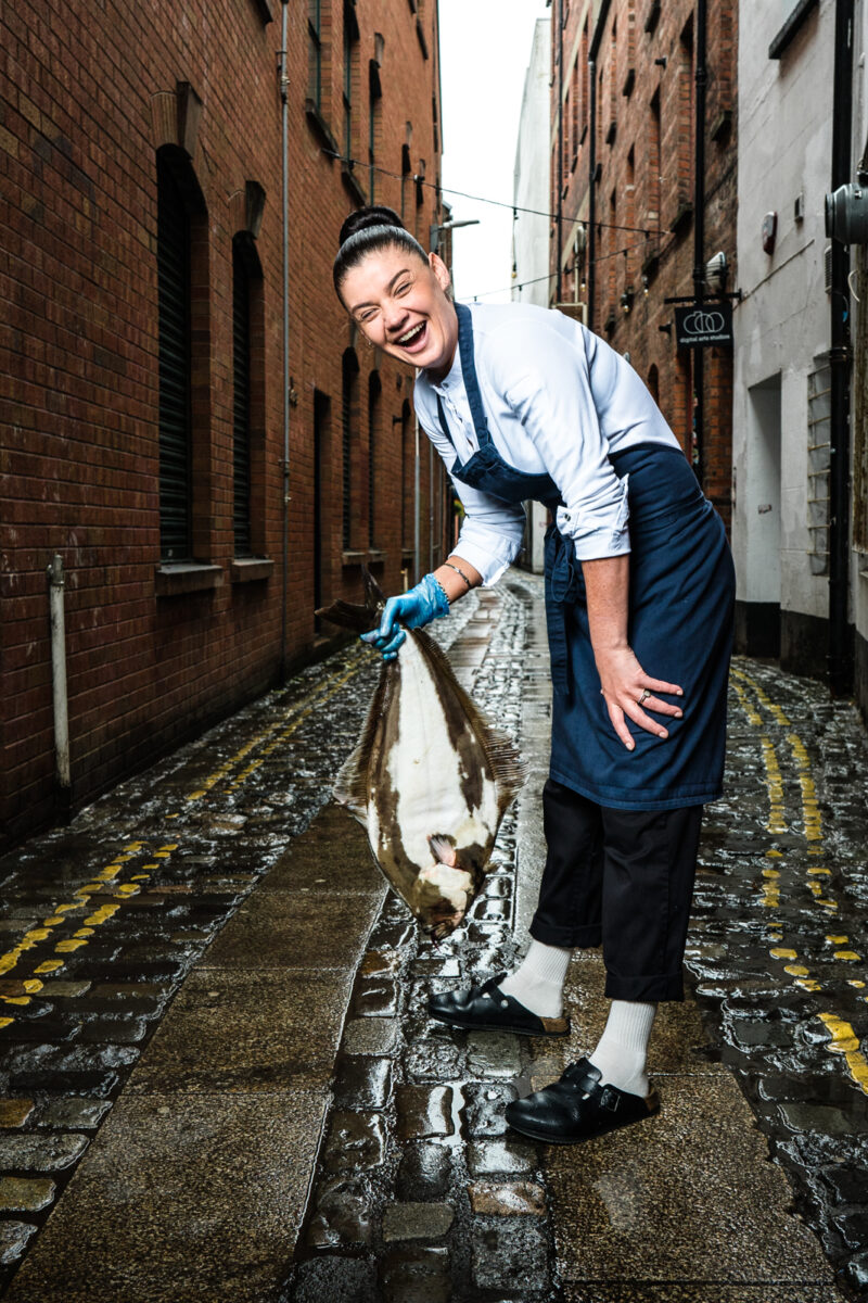 Chef Lottie Noren laughing with halibut. Photography: Elaine Hill, Belfast, Northern Ireland. - Chef Lottie Noren; Beau Restaurant Belfast with halibut in Cathedral Quarter